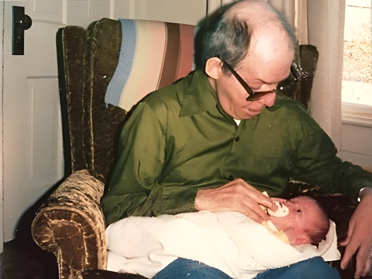 Francis Gauthier in an armchair feeding a newborn (vintage family photo)